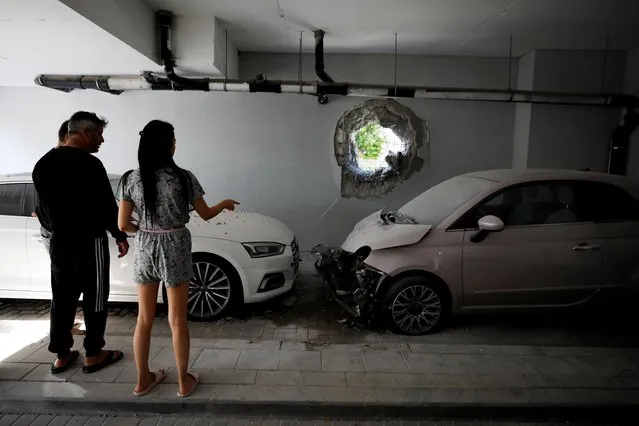 Residents look at their cars at the parking area under a residential building in Ashkelon, Israel, which was damaged by a direct hit from a rocket launched overnight from the Gaza Strip May 14, 2021. (Photo by Amir Cohen/Reuters)