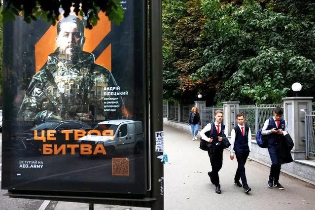 School-aged boys walk past a poster calling on people to sign up for the army in Kyiv on September 20, 2023. (Photo by Thomas Peter/Reuters)