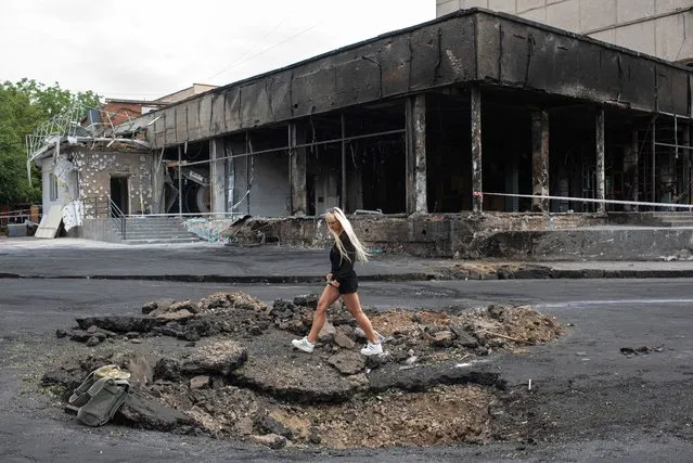 A young woman walks over a hole made by a rocket on July 15, 2022 in Vinnytsia, Ukraine. Scores of people were also wounded in the attack, in which rockets hit a multistory building in the city's center. Vinnytsia had not been the target of significant attacks since early March. (Photo by Alexey Furman/Getty Images)