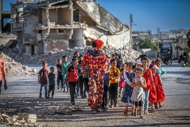 Children enjoy their time with a volunteer wearing a clown costume during the Eid al-Adha in the village of Nayrab, Idlib, Syria on June 10, 2022. 50 children attended a holiday event, where theatrical performances and many activities including sports, dances and riddles were held in the destroyed village. (Photo by Muhammed Said/Anadolu Agency via Getty Images)