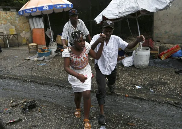 A Haitian couple jumps over running wastewater in Port-au-Prince, Haiti, Friday, July 9, 2021, two days after Haitian President Jovenel Moise was assassinated in his home. (Photo by Fernando Llano/AP Photo)