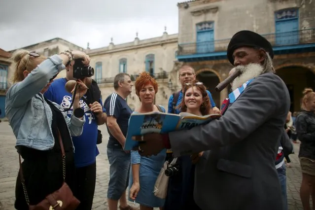 Hermenegildo Arensivia, 61, (R), shows pictures of him in a magazine to tourists from Poland in old Havana in this January 13, 2016 picture. (Photo by Alexandre Meneghini/Reuters)