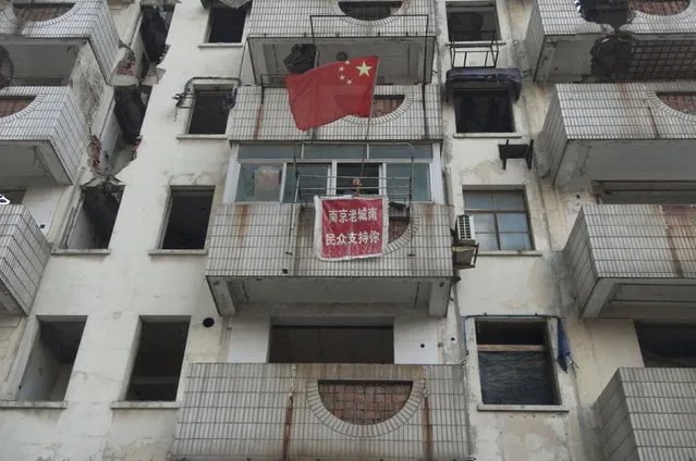 Xu Aiguo, the owner of a nail house, the last house in the area, set up a Chinese national flag outside his balcony in Nanjing, Jiangsu province, China, November 8, 2010. (Photo by Reuters/Stringer)