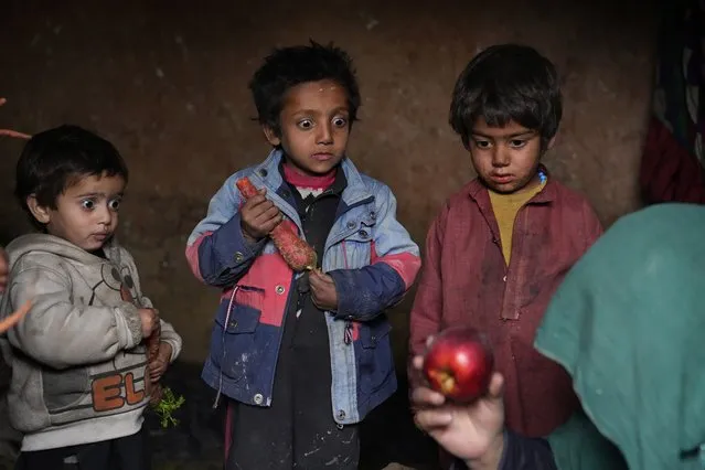Three internally displaced children look with surprise at an apple that their mother brought home after begging, in a camp on the outskirts of Kabul, Afghanistan, Thursday, February 2, 2023. Since the chaotic Taliban takeover of Kabul on Aug. 15, 2021, an already war-devastated economy once kept alive by international donations alone is now on the verge of collapse. (Photo by Ebrahim Noroozi/AP Photo)