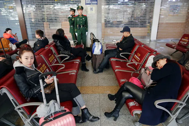 Paramilitary policemen stand behind passengers waiting at the departure hall of the Beijing Railway Station in central Beijing, as China gears up for Lunar New Year, when hundreds of millions of people head home, in Beijing, China January 27, 2017. (Photo by Damir Sagolj/Reuters)