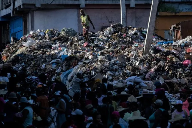 Market goers walk past as a man salvages goods from a mound of garbage at the Marche Lacoupe market in Port-au-Prince, Haiti on October 24, 2021. (Photo by Adrees Latif/Reuters)