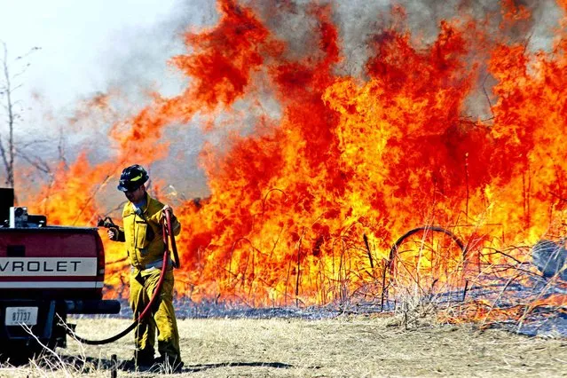 In this photo taken on Monday, March 16, 2015, a firefighters works to contain a grass fire north of Honey Creek, Iowa. Officials say the large grass fire in western Iowa was caused by what was meant to be a controlled burn. (Photo by Mike Bell/AP Photo/The Daily Nonpareil)