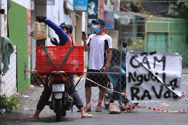 A delivery man hands over food order to another at a fence set up block traffic in Vung Tau, Vietnam, Monday, September 13, 2021. The sign at right reads “No non-resident”. (Photo by Hau Dinh/AP Photo)