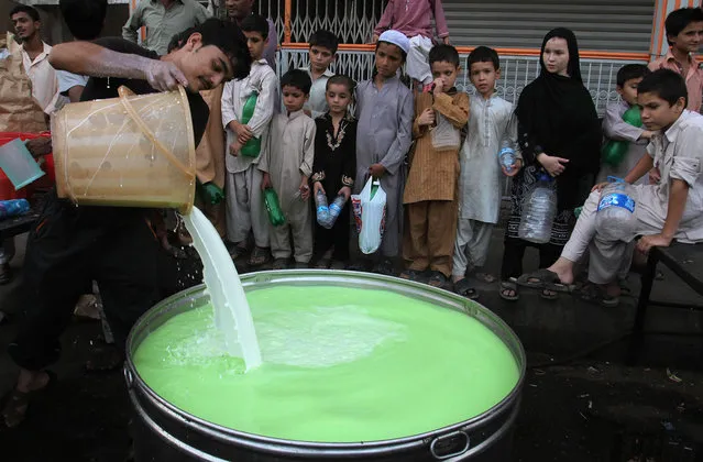 Pakistani children wait to receive milk mixed with fruit juice to break the day's fast that many Muslims practice during the month of Ramadan in Karachi, Pakistan, Friday, July 3, 2015. Muslims across the world are observing the holy fasting month of Ramadan, where they refrain from eating, drinking and smoking from dawn to dusk. (Photo by Fareed Khan/AP Photo)