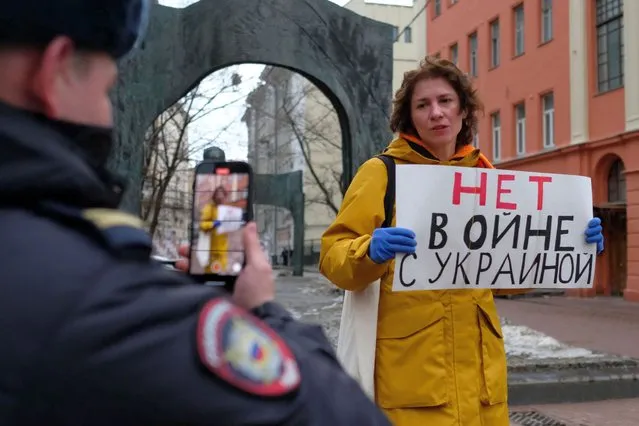A police officer uses his smartphone to film a woman staging a picket with a placard reading “No to war with Ukraine“ in Moscow on February 23, 2022. (Photo by Nikolay Korzhov/AFP Photo)