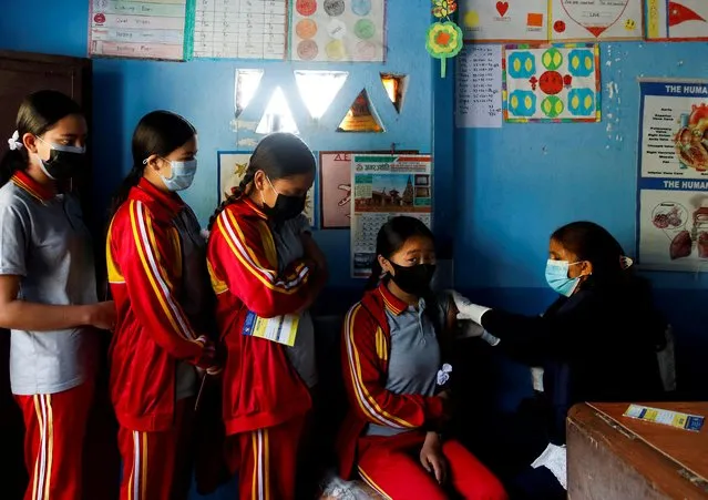 Students wait in a queue as their friend receives a dose of the Moderna vaccine against the coronavirus disease (COVID-19), at their school during a vaccination drive for children aged 12-17 in Bhaktapur, Nepal, January 9, 2022. (Photo by Navesh Chitrakar/Reuters)