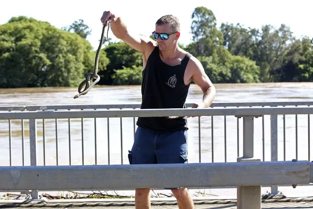 A man handles a python snake searching for dry ground on a bridge in Logan, south of Brisbane, Australia, Tuesday, March 1, 2022. Tens of thousands of people had been ordered to evacuate their homes by Tuesday and many more had been told to prepare to flee as parts of Australia's southeast coast are inundated by the worst flooding in decades. (Photo by Jono Searle/AAP Image via AP Photo)