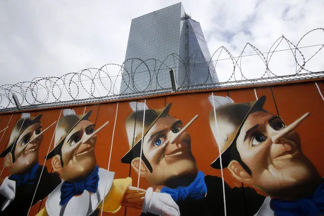 Graffiti is painted on a fence around the construction site of the new headquarters of the European Central Bank in Frankfurt, Germany, Wednesday, May 7, 2014. The ECB is supposed to move into the building by the end of 2014. The Governing Council of the ECB will meet on Thursday. The graffito was created by German street artist “Case”. He painted a repetition of 16 Pinocchio's puppets on the wood panels surrounding the construction site of the new headquarters of the European Central Bank. (Photo by Michael Probst/AP Photo)