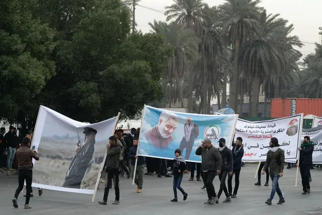 Supporters and members of the Popular Mobilization Forces hold posters of a powerful Iranian general and a top Iraqi militia leader in Baghdad, Iraq, Saturday, January 1, 2022. Hundreds rally in Baghdad on Soleimani assassination anniversary, chanting anti-American slogans, hundreds of people rallied in in the Iraqi capital on the first day of the year Saturday to mark the anniversary of the killing of a powerful Iranian general and a top Iraqi militia leader in a U.S. drone strike. (Photo by Khalid Mohammed/AP Photo)