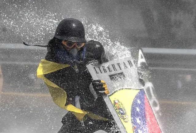 An oposition demonstrators is hit by the jet from a riot police water cannon during a protest against President Nicolas Maduro in Caracas, on May 10, 2017. Venezuelan protesters hit the streets on Wednesday armed with “Poopootov cocktails”, jars filled with excrement which they vowed to hurl at police as a wave of anti-government demonstrations turned dirty. (Photo by Juan Barreto/AFP Photo)