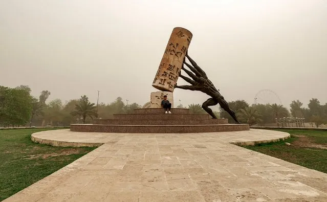 A youth sits by the “Saving Iraqi Culture” monument at the Mansour district of Iraq's capital Baghdad during a severe dust storm on April 20, 2022. The monument, commissioned in 2010 and designed by Iraqi sculptor Mohammed Ghani Hikmat, depicts a broken cylinder seal with cuneiform script reading “writing began here” with hands and arms attempting to support it from falling. (Photo by AHmad Al-Rubaye/AFP Photo)