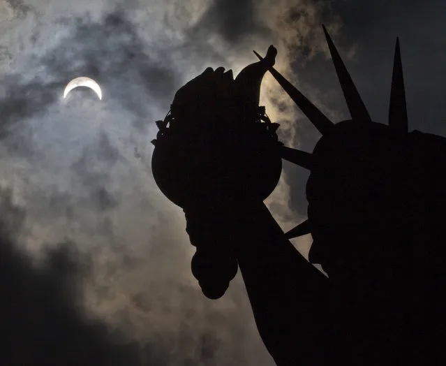 A partial solar eclipse appears over the Statue of Liberty on Liberty Island in New York, Monday, August 21, 2017. (Photo by Seth Wenig/AP Photo)