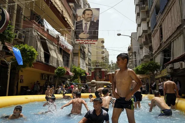 Children swim in an inflatable pool that supporters of former Prime Minister Saad Hariri installed to illustrate their intention to boycott parliamentary elections, in Beirut, Lebanon, Sunday, May 15, 2022. Hariri, seen in poster, suspended his participation in Lebanese politics last year and has called on supporters to boycott Sunday’s vote – the first since Lebanon’s implosion started in October 2019. (Photo by Hassan Ammar/AP Photo)