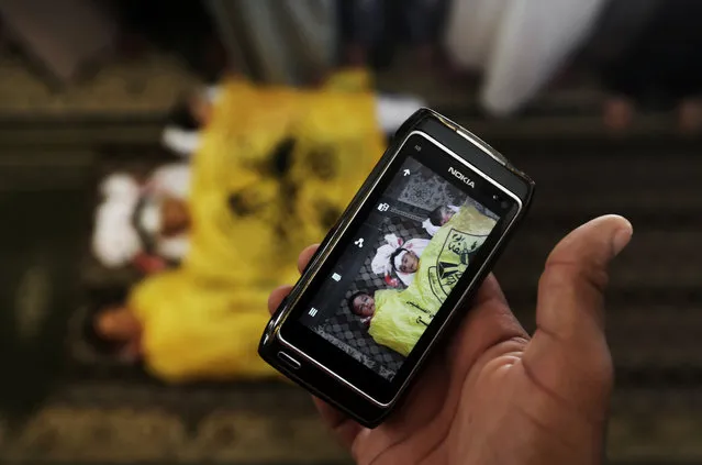 A man takes a photo with his mobile phone of the lifeless bodies of Qasim Alwan, 4, Imad Alwan, 6, and Rizk Hayek, 1, who were killed Friday by an Israeli tank shell, during their funeral in Gaza City, Saturday, July 19, 2014. (Photo by Hatem Moussa/AP Photo)