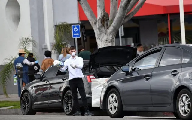 A man offers toilet paper and paper towels for free (1 roll per family) from the back of his car in Los Angeles on March 24, 2020. Some 1.7 billion people have been asked to stay home in over 50 countries and territories around the world as governments battle the coronavirus pandemic sweeping the globe, according to an AFP tally March 23. (Photo by Chris Delmas/AFP Photo)
