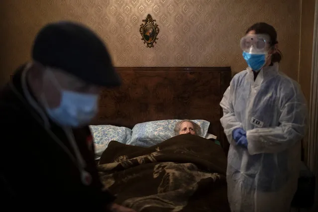 Josefa Ribas, 86, who is bedridden, looks at nurse Alba Rodriguez as Ribas' husband, Jose Marcos, 89, stands by in their home in Barcelona, Spain, March 30, 2020, during the coronavirus outbreak. Ribas suffers from dementia, and Marcos fears for them both if the virus enters their home. “If I get the virus, who will take care of my wife?”. (Photo by Emilio Morenatti/AP Photo)
