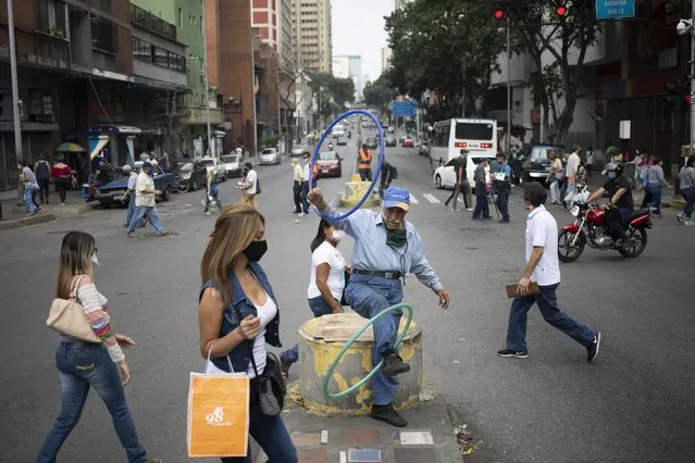 Street juggler Jose Bestilleiro, 86, performs as pedestrians, some wearing face masks as a measure to curb the spread of the new coronavirus, walk past in downtown Caracas, Venezuela, Saturday, June 20, 2020, during a relaxation of restrictive measures amid the new coronavirus pandemic. (Photo by Ariana Cubillos/AP Photo)