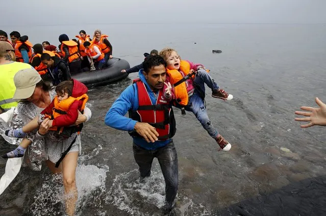 A volunteer helps Syrian refugee carry one of his two children off an overcrowded dinghy at a beach after crossing part of the Aegean Sea from Turkey to the Greek island of Lesbos September 23, 2015. (Photo by Yannis Behrakis/Reuters)