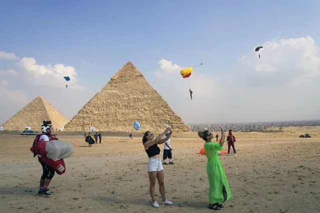 Tourists film parachutists as they approach the historical site of the Giza Pyramids, near Cairo, Egypt, Wednesday, November 2, 2022.  More than 100 parachutists from 16 countries are participating at “Jump Like a Pharaoh” festival at the site of Giza Pyramids ahead of COP27 to be held in Egypt in November 6. (Photo by Amr Nabil/AP Photo)