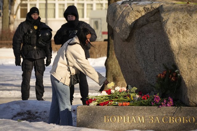 Police officers watch a woman laying flowers to pay tribute to Alexei Navalny at the monument, a large boulder from the Solovetsky islands, where the first camp of the Gulag political prison system was established in St. Petersburg, Russia, Sunday, February 18, 2024. Russians across the vast country streamed to ad-hoc memorials with flowers and candles to pay tribute to Alexei Navalny, the most famous Russian opposition leader and the Kremlin's fiercest critic. Russian officials reported that Navalny, 47, died in prison on Friday. (Photo by Dmitri Lovetsky/AP Photo)