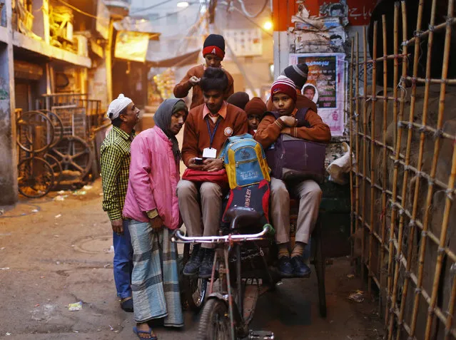A schoolboy shows his mobile phone to a rickshaw puller taking him and other students to school on a cold winter morning in the old quarters of Delhi January 30, 2014. (Photo by Anindito Mukherjee/Reuters)