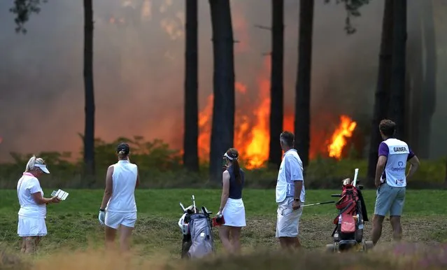 Players, Sophie Powell, Cara Gainer and Gabriella Cowley and their caddies look on as a fire nears the 10th hole during day three of The Rose Ladies Series on The West Course in the first ever ladies professional event at Wentworth Golf Club on August 07, 2020 in Virginia Water, England. (Photo by Naomi Baker/Getty Images)