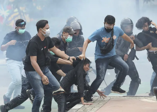 Amid tear gas clouds, plain-clothed police officers detain protesters during a rally in Jakarta, Indonesia, Thursday, October 8, 2020. Thousands of enraged students and workers staged rallies across Indonesia on Thursday in opposition to a new law they say will cripple labor rights and harm the environment. (Photo by Tatan Syuflana/AP Photo)