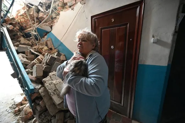 Tamara Skliarova, 70, holds a cat in front of debris in a stairwell of a two-storey residential building where she lives, which was partially destroyed as a result of Russian shelling in Kupiansk, Kharkiv region on February 13, 2023. (Photo by Sergey Bobok/AFP Photo)