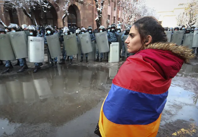 A woman wearing a state Armenian flag stands in front of a riot police line during a rally to pressure Armenian Prime Minister Nikol Pashinyan to resign over a peace deal with neighboring Azerbaijan on Republic Square in Yerevan, Armenia, Thursday, December 24, 2020. (Photo by Vahram Baghdasaryan, Photolure via AP Photo)