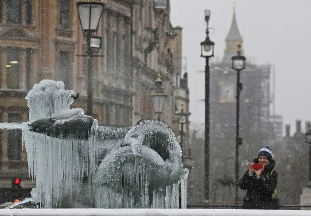 A woman takes pictures of icicles on the fountain in Trafalgar Square with the background of Big Ben as temperatures dropped below freezing in London, Tuesday, February 9, 2021. Snow has swept across the country, with further snowfall predicted, bringing travel problems as temperatures dropped. (Photo by Frank Augstein/AP Photo)