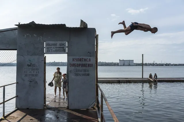 A man dives off a gate on a partiality submerged dock on the Southern Buh River in Mykolaiv, Ukraine, June 8, 2023. President Volodymyr Zelensky of Ukraine visited the flood-stricken city of Kherson on Thursday, trying to rally the region’s emergency workers, struggling under Russian artillery fire, to evacuate thousands of people from cities and settlements left submerged by the destruction of a major dam this week. (Photo by Brendan Hoffman/The New York Times)