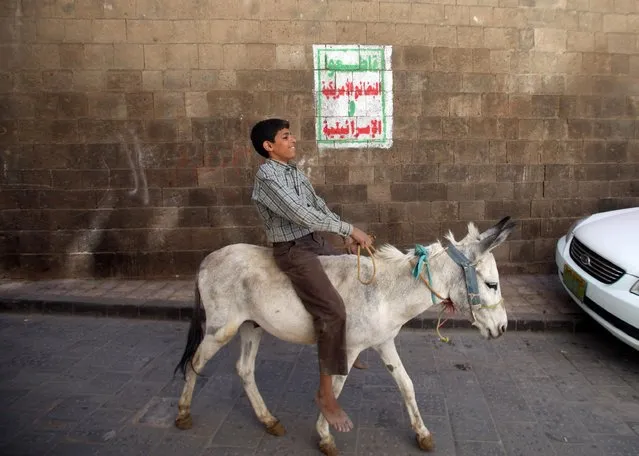 A boy rides his donkey past a sign painted on a wall with the main motto of the Shi'ite Houthi movement in the old quarter of Sanaa, Yemen January 31, 2015. The sign reads, “Boycott the American and Israeli products!”. (Photo by Mohamed al-Sayaghi/Reuters)