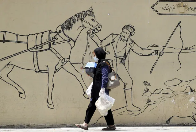 An Iranian woman carries her belongings as she walks next to a wall painting in a street in Tehran, Iran, 12 June 2023. Iran's Supreme Leader Ali Khamenei said on 11 June during a meeting with Iranian nuclear scientists, that the West could not stop Iran's nuclear progress, as he urged continued cooperation with the International Atomic Energy Agency (IAEA), amidst the scrutiny from Western powers on the country's nuclear programme. (Photo by Abedin Taherkenareh/EPA/EFE)