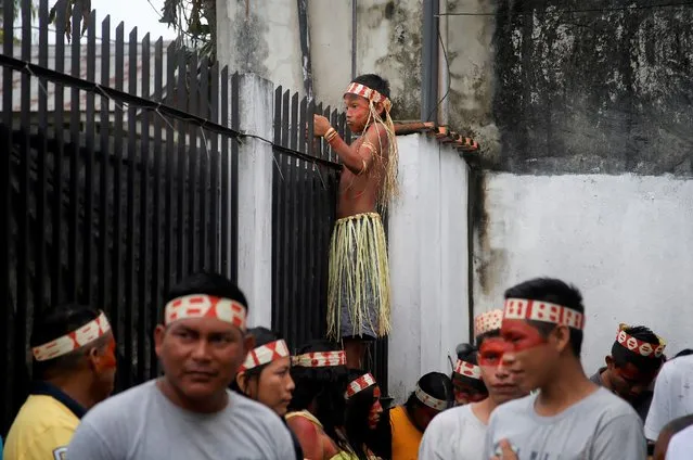 A Mayuruna Indigenous boy climbs a fence to look at the march against the disappearance of Indigenous expert Bruno Pereira and freelance British journalist Dom Phillips, in Atalaia do Norte, Vale do Javari, Amazonas, state Brazil, Monday, June 13, 2022. Brazilian police are still searching for Pereira and Phillips, who went missing in a remote area of Brazil's Amazon a week ago. (Photo by Edmar Barros/AP Photo)