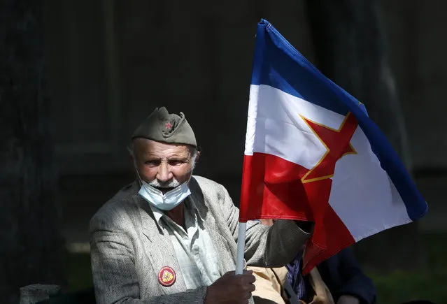 A supporter of the late Yugoslav communist president Josip Broz Tito holds an old Yugoslav flag with the communist five-point star in front of memorial complex prior a wreath laying ceremony in Belgrade, Serbia, Tuesday, May 25, 2021. Some people have gathered at Tito's grave to mark the 129th anniversary of his birth. (Photo by Darko Vojinovic/AP Photo)