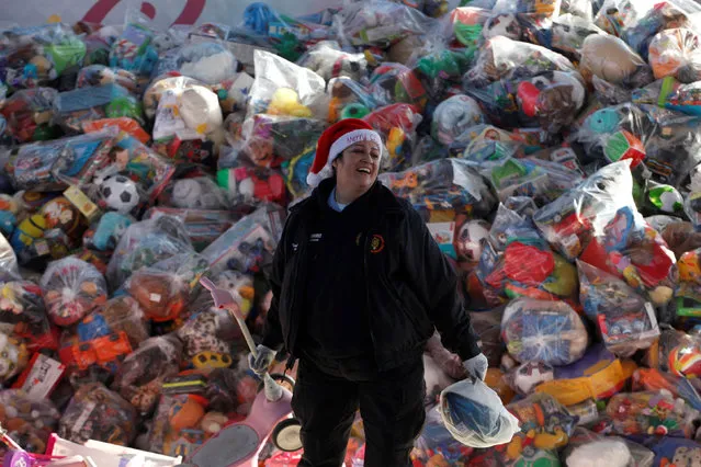 A volunteer smiles as she stands next to bags with toys during an annual gift-giving event organised by firefighters, who collect donated toys throughout the year and hand them out to needy children on Christmas eve, in Ciudad Juarez, Mexico, December 24, 2016. (Photo by Jose Luis Gonzalez/Reuters)