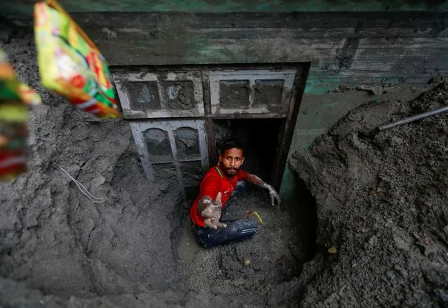 A man works to retrieve belongings from a house partially submerged in mud after the area was hit by flash floods along the bank of Melamchi River in Sindhupalchok, Nepal on June 20, 2021. (Photo by Navesh Chitrakar/Reuters)