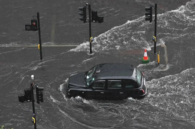 A London taxi drives through water on a flooded road in The Nine Elms district of London on July 25, 2021 during heavy rain. Thunder storms and heavy rain caused flash flooding around the British capital on July 25. (Photo by Justin Tallis/AFP Photo)