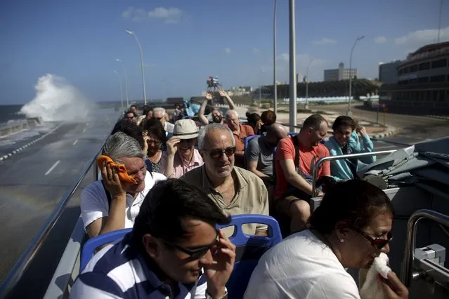 Tourists on top of a double decker sightseeing bus, take cover against the crashing waves at the seafront Malecon in Havana in this January 17, 2016 picture. (Photo by Alexandre Meneghini/Reuters)