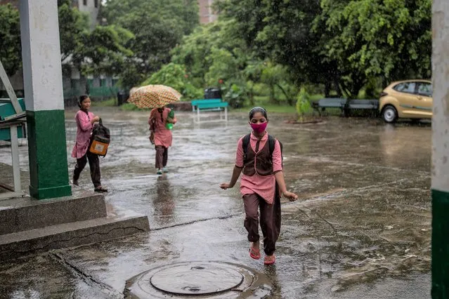 Students arrive at a school amid heavy downpour on the first day of partial reopening of schools in Noida, a suburb of New Delhi, India, Wednesday, September 1, 2021. Many students in India will be able to step inside a classroom for the first time in nearly 18 months from Wednesday, as authorities have given the green light to partially reopen schools despite apprehension from some parents and signs that coronavirus infections are picking up again. Schools and colleges in least six states will reopen in a gradual manner with health measures in place throughout September. In New Delhi, all staff must be vaccinated and class sizes will be capped at 50% with staggered seating and sanitized desks. (Photo by Altaf Qadri/AP Photo)