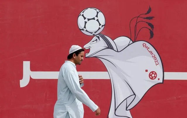 A man walks past a poster of the Qatar 2022 mascot La'eeb in Doha on November 9, 2022, ahead of the Qatar 2022 FIFA World Cup football tournament. (Photo by Odd Andersen/AFP Photo)