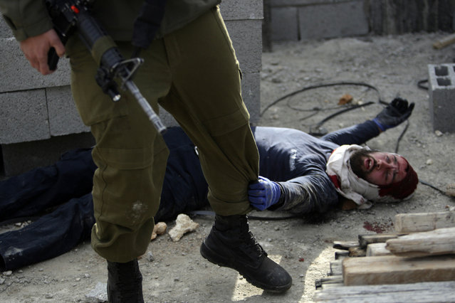 An injured Israeli settler grabs an Israeli soldier's leg to get his attention after the settler was detained by Palestinian villagers in a building under construction near the West Bank village of Qusra, January 7, 2014. (Photo by Nasser Ishtayeh/AP Photo)