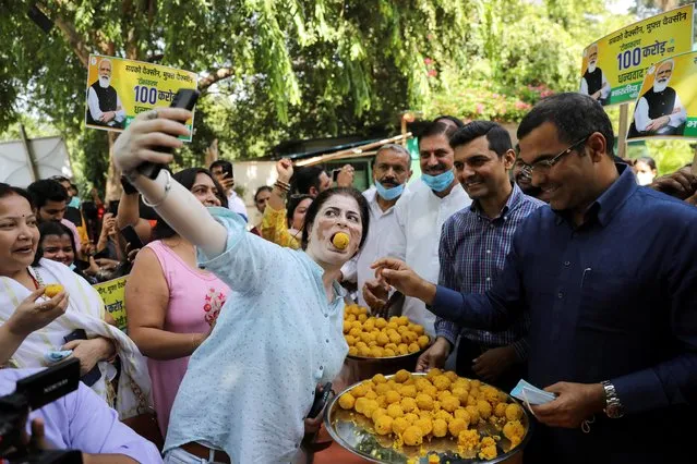 A woman takes a selfie while being fed with sweets as India celebrates the milestone of administering one billion COVID-19 vaccine doses, at an event organised by members of India's ruling Bharatiya Janata Party (BJP) in New Delhi, India, October 21, 2021. (Photo by Anushree Fadnavis/Reuters)