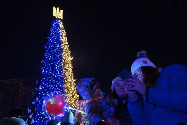 People take selfie photographs during the unveiling ceremony of Kyiv's main Christmas tree  on St. Sophia Square in the Ukrainian capital of Kyiv, on December 19, 2022. Drones attacked the Ukrainian capital early on December 19, 2022 morning, the Kyiv city military administration said, urging people to heed air alerts. (Photo by Sergei Supinsky/AFP Photo)