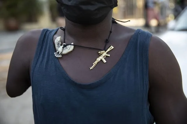 A man wearing a necklace adorned with charms depicting a phoenix and a machine gun, waits for faithful to exit the Saint Peter's Catholic church to beg for alms, in Port-au-Prince, Haiti, Tuesday, September 28, 2021. (Photo by Rodrigo Abd/AP Photo)